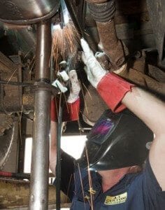 A technician welding a muffler with sparks flying. 